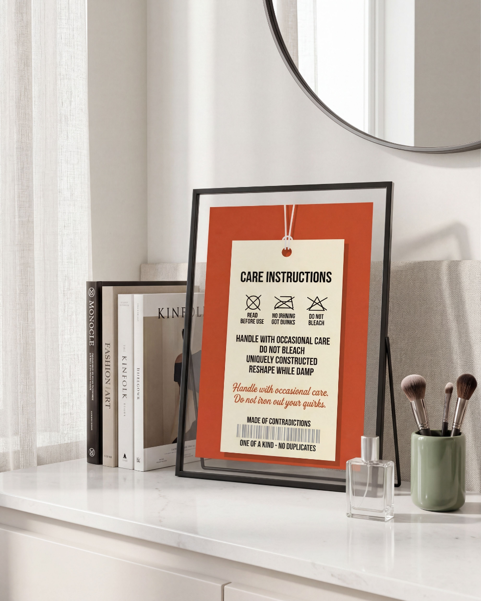 handle with care Poster Graphic illustration of a vintage cream-colored clothing care tag hanging by a white string against a burnt orange background. The text reads "Care Instructions", "Read Before Use", "No Ironing Out Quirks", "Do Not Bleach", and "Made of Contradictions" with matching playful laundry icons.